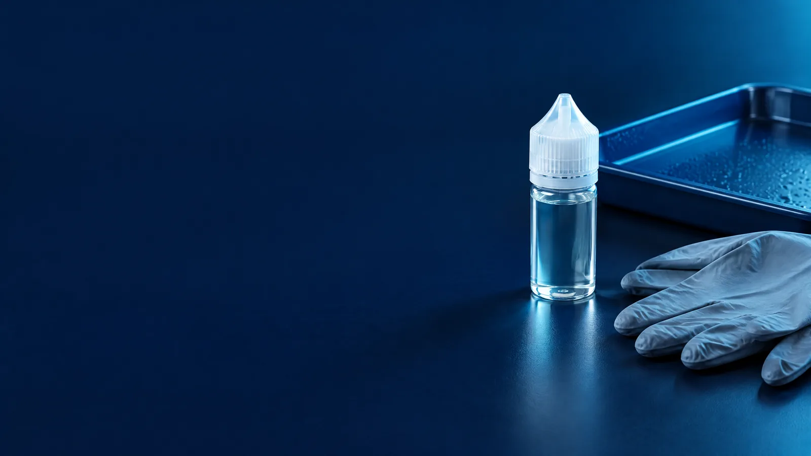 Unbranded vaping-liquid bottle with a closed cap, protective gloves and a waterproof tray arranged on a dark blue safety work surface.